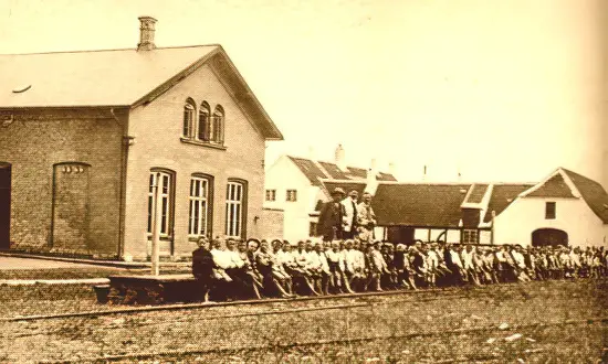 Billede af cirka 100 drenge på stationens perron, senest 1914. Til venstre stationsbygningen, længere tilbage opsynsmandens bolig.