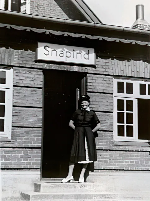 Billede af Snapind Holdeplads med "stationsforstander" Tove Andersen, der havde været bestyrer fra den 1. april 1954 til banens lukning, hvor Tove Andersen fortsatte som bestyrer af posthuset til den 31. marts 1967.