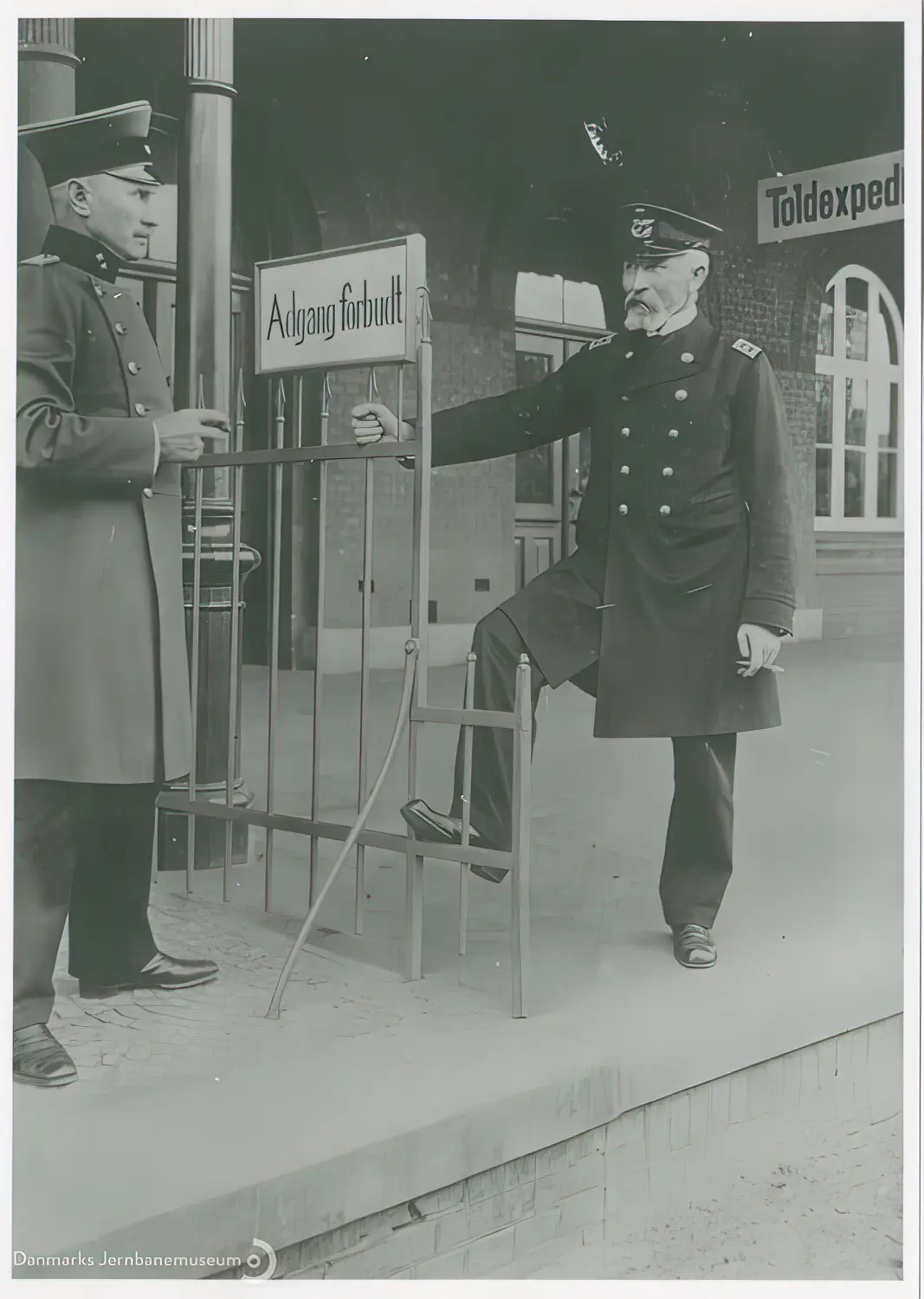 Bahnhofsvorsteher Johan Friedrich Wilhelm Ehlers og stationsforstander Jens Jensen Høgdal i en cigarpassiar på tværs af perronens grænsestakit.