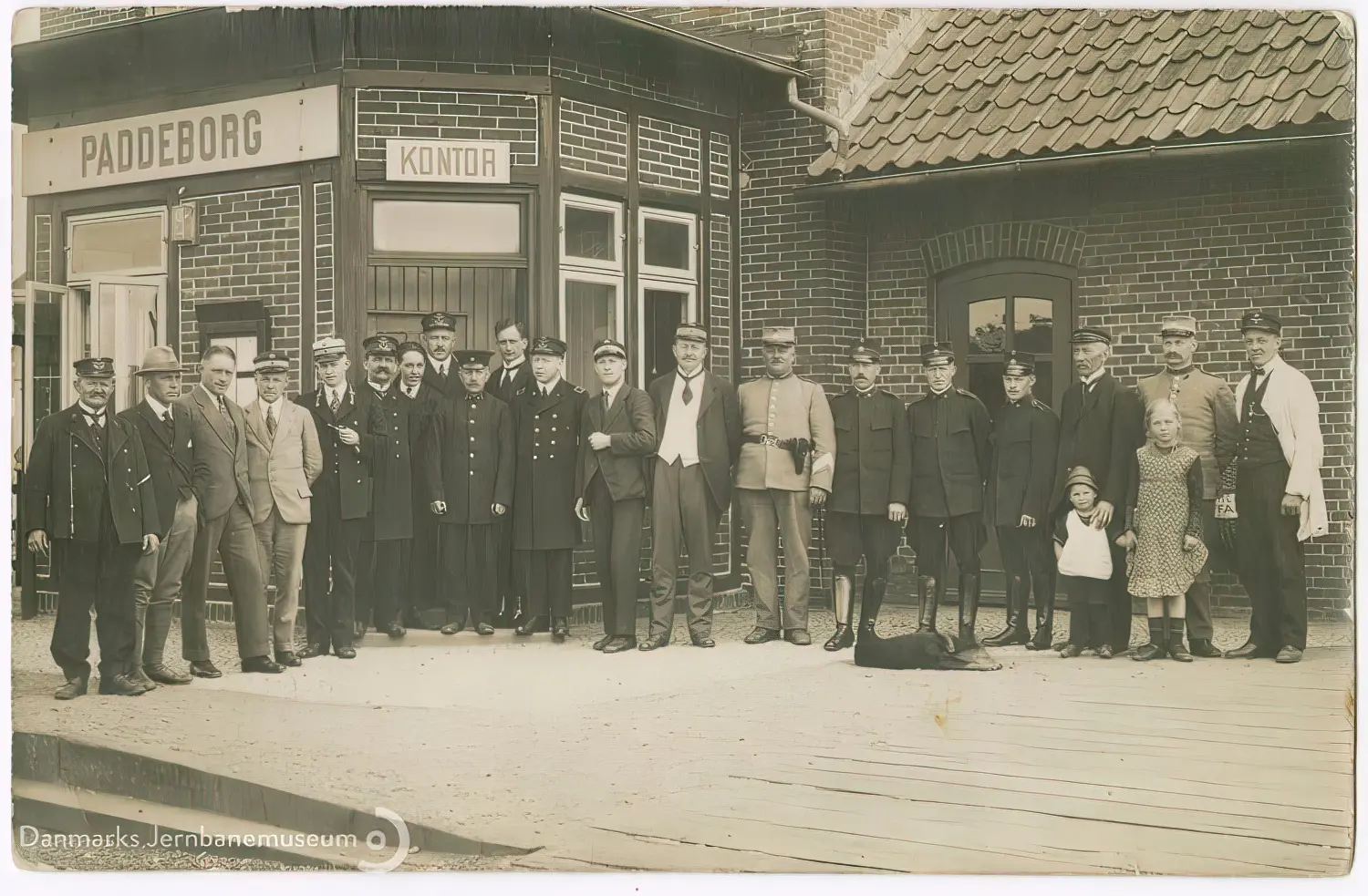 Civile, toldere, politi, gendarmer og en enkelt tysk tjenestemand på perronen under det nye danske stationsnavneskilt efter den danske overtagelse af stationen natten mellem den 16. og 17. jun. 1920.