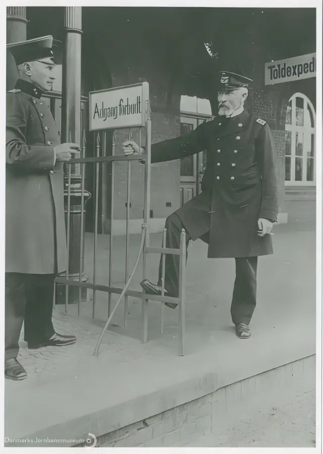 Billede af bahnhofsvorsteher Johan Friedrich Wilhelm Ehlers og stationsforstander Jens Jensen Høgdal i en cigarpassiar på tværs af perronens grænsestakit på Vedsted-Hvidding Station.